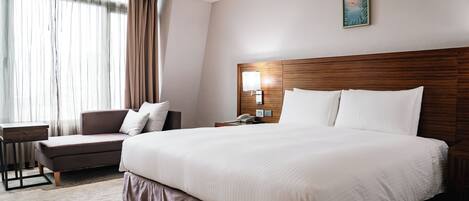 Una habitación de hotel con una cama grande, un escritorio, una silla y un ventanal con cortinas.