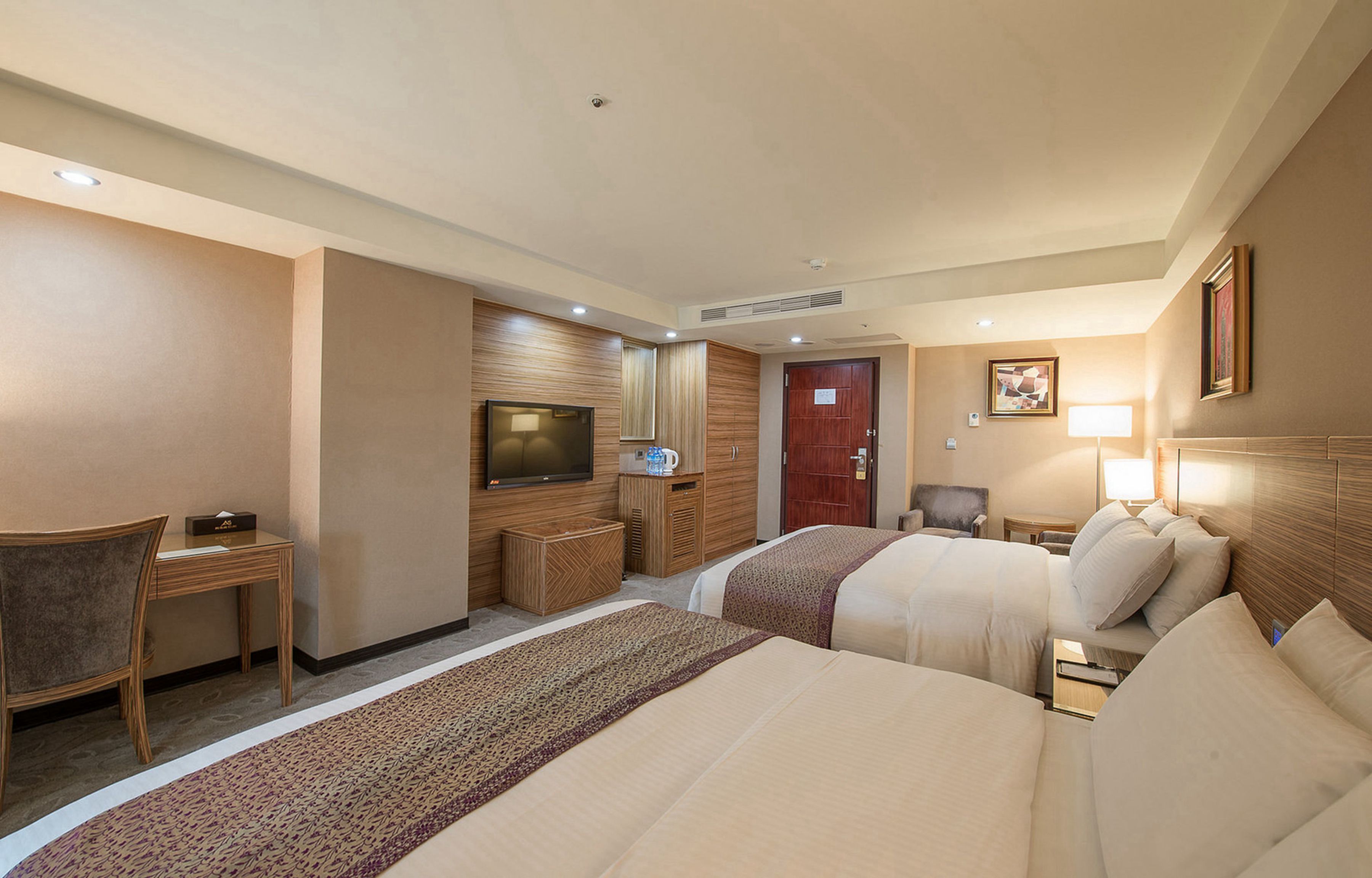 A hotel room with two beds, a desk, a television, a wardrobe, and a door.