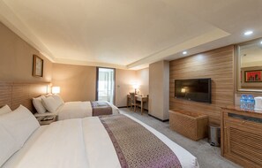 A hotel room with two beds, a desk, a TV, and a minibar.