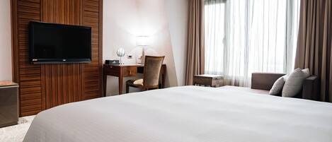 Une chambre d’hôtel avec un grand lit, un bureau avec une chaise, un téléviseur fixé au mur et une fenêtre avec des rideaux.