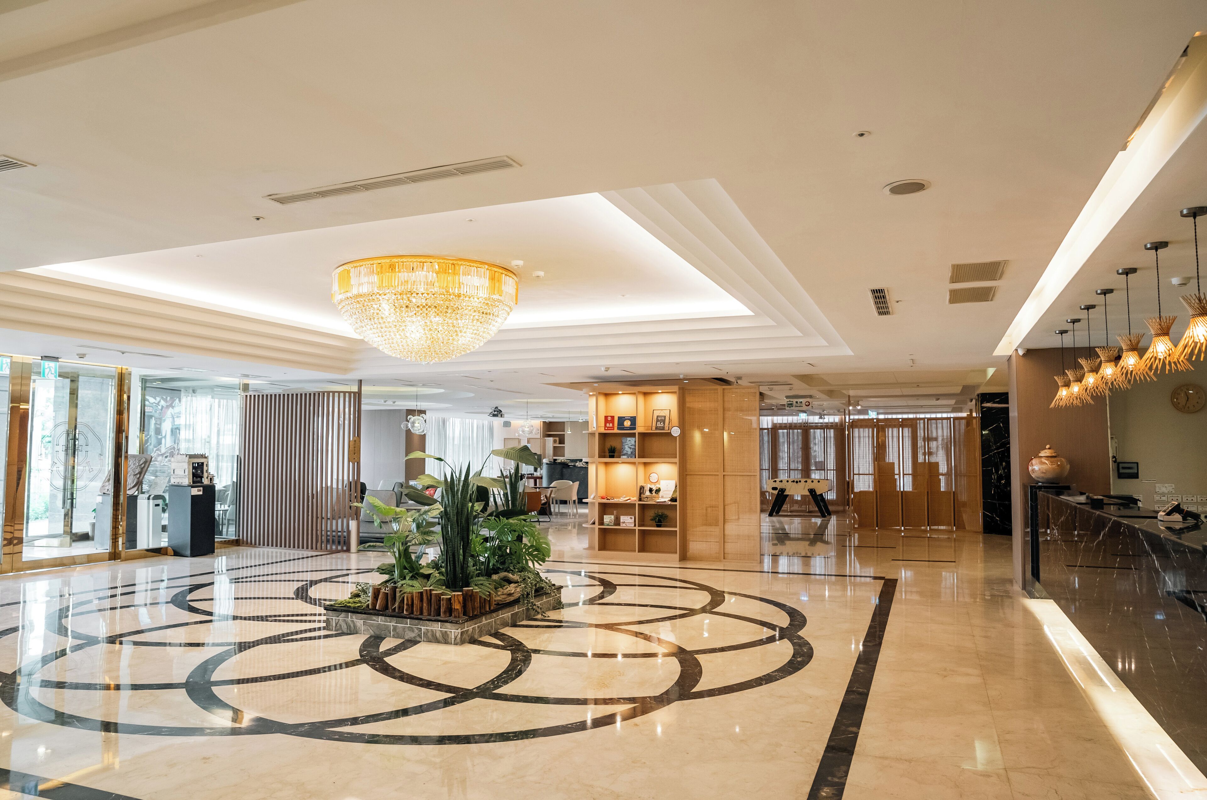 A spacious lobby with a central circular marble floor, a large chandelier, and a reception desk.