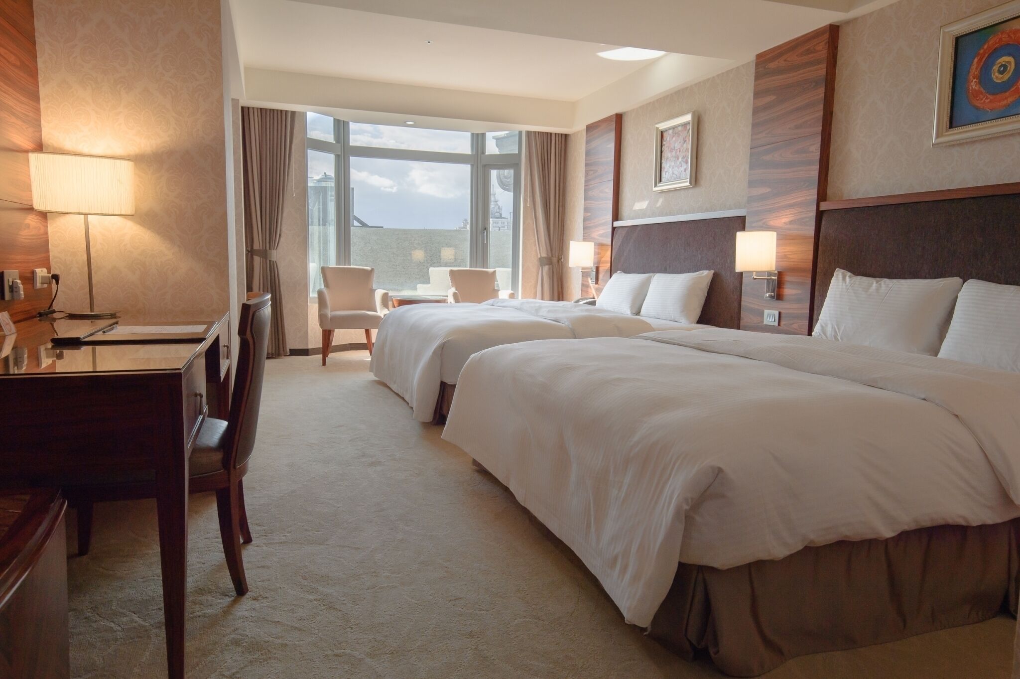 A hotel room with two beds, a desk, and a chair.