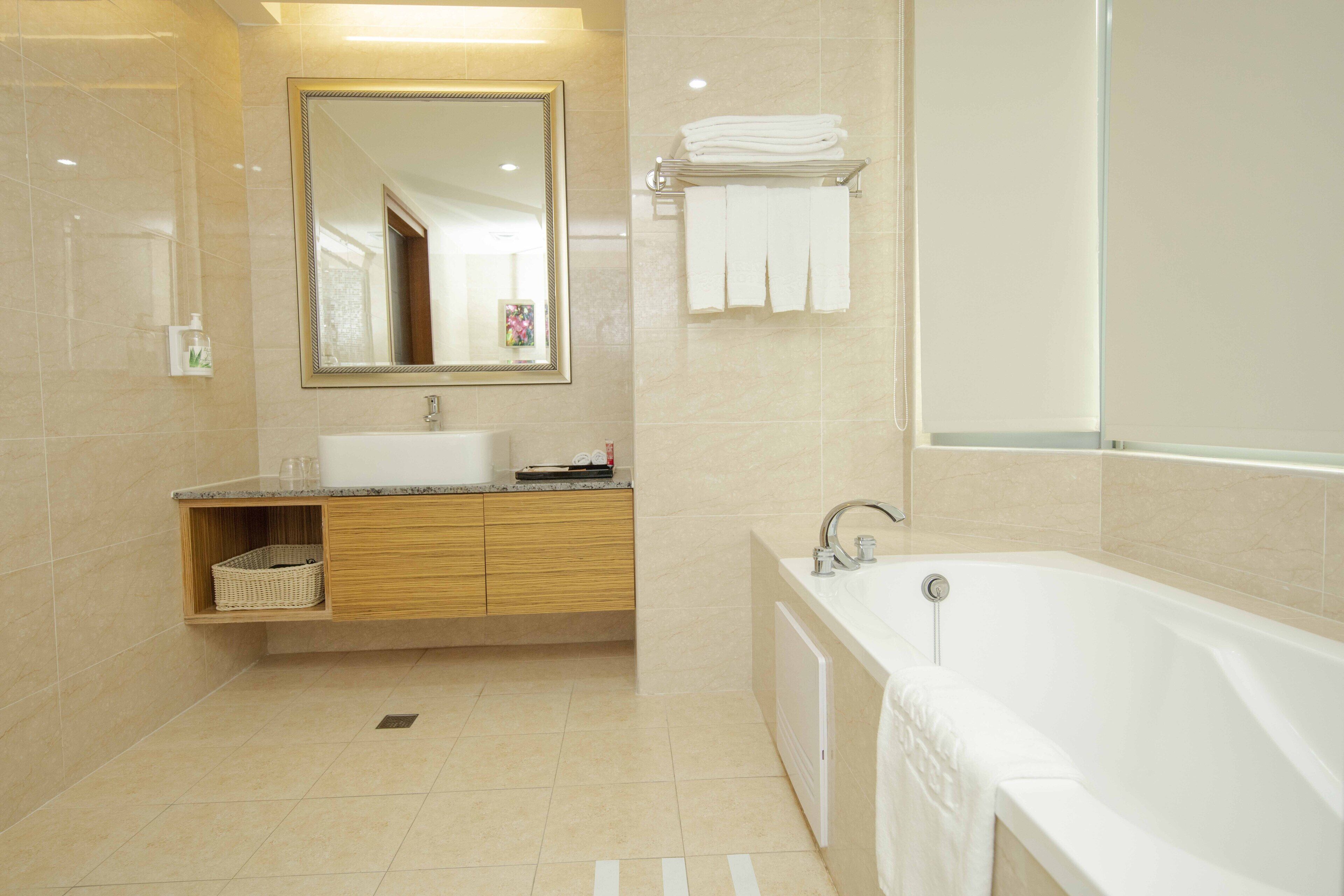A modern bathroom with a large mirror, a bathtub, a sink, and a towel rack.