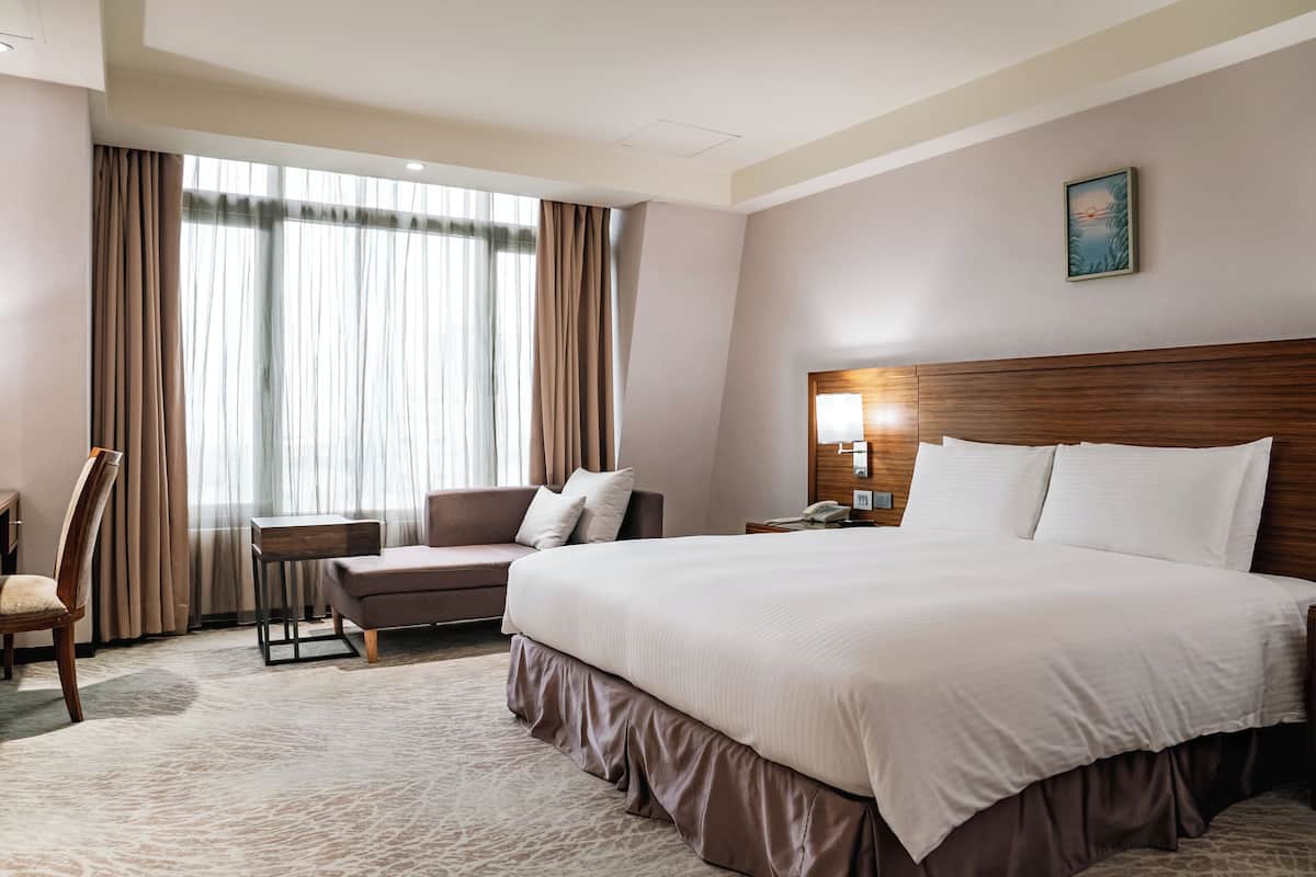 Une chambre d’hôtel avec un grand lit, un bureau, une chaise et une fenêtre avec des rideaux.