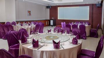 A conference room with round tables, purple chair covers, and a large screen.