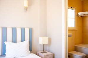 Habitación de hotel con cama, mesita de noche con lámpara, baño con inodoro y toallero.