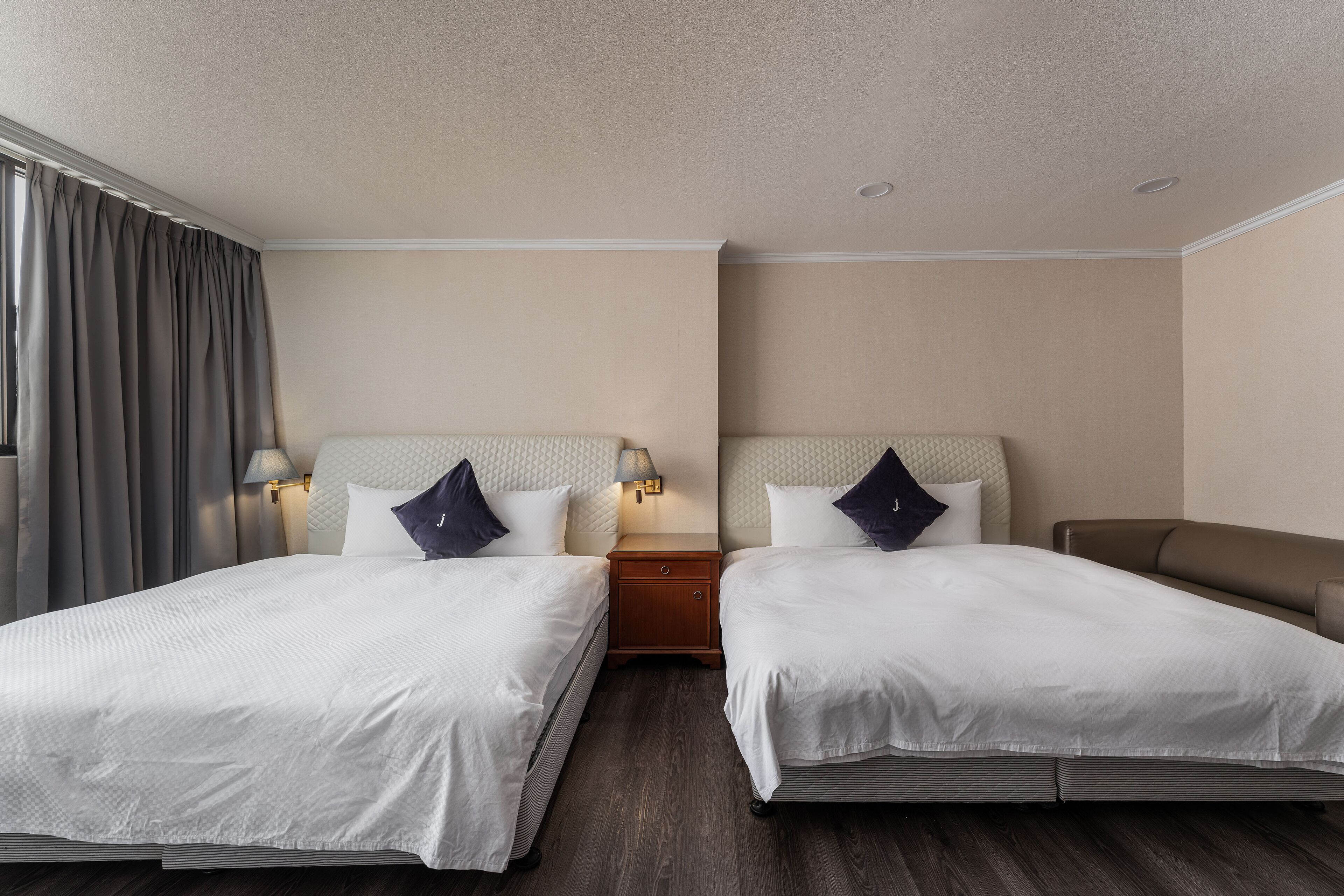 A hotel room with two beds, a nightstand, and a lamp.