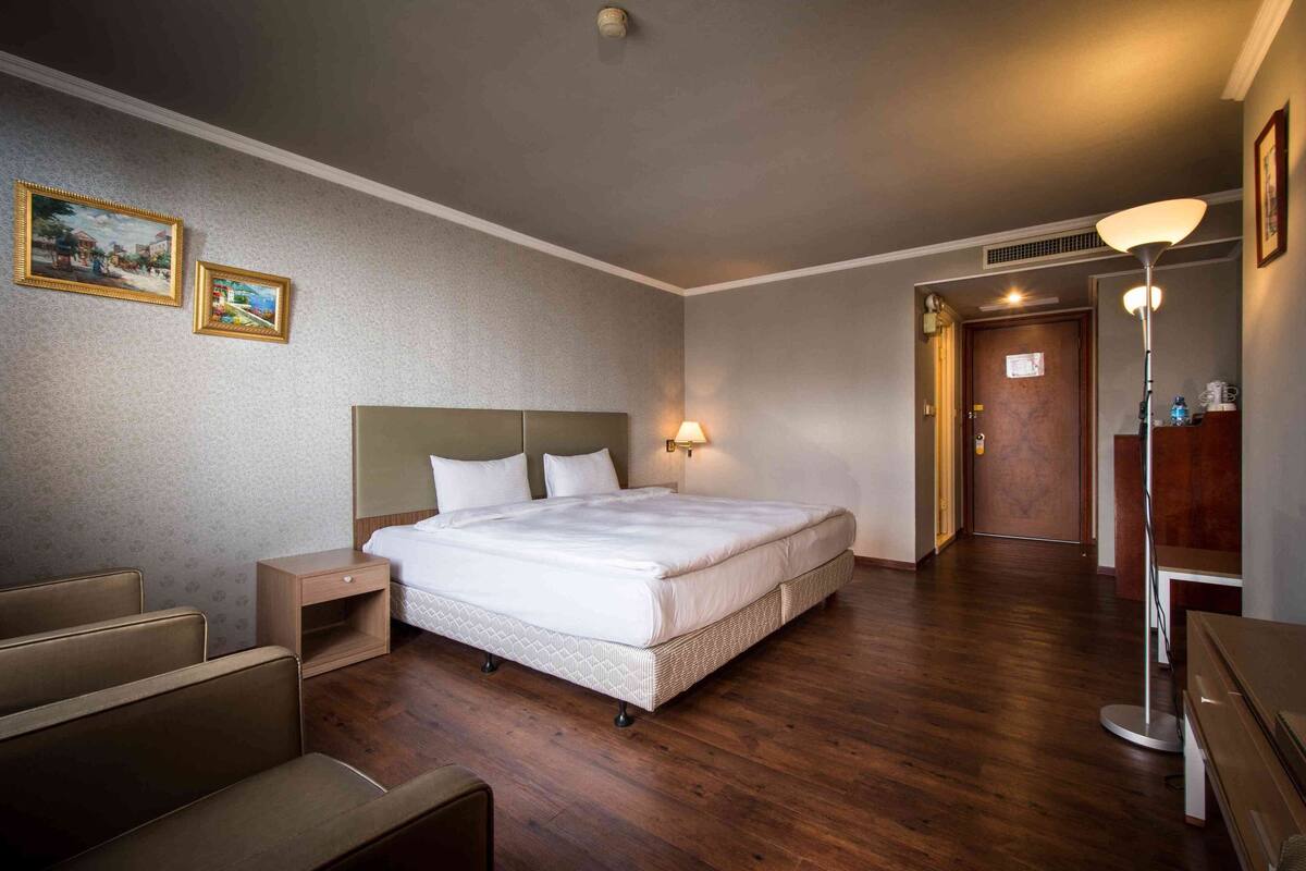 A hotel room with a bed, bedside tables, a lamp, a desk, and a chair.