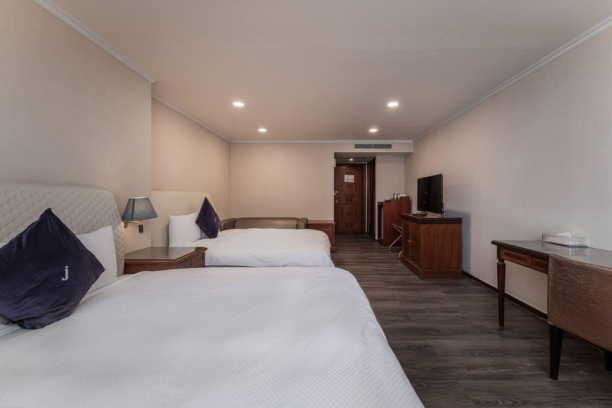 A hotel room with two beds, a desk, a TV, and a bathroom visible through an open door.