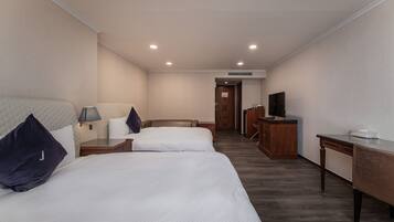 A hotel room with two beds, a desk, a TV, and a bathroom visible through an open door.