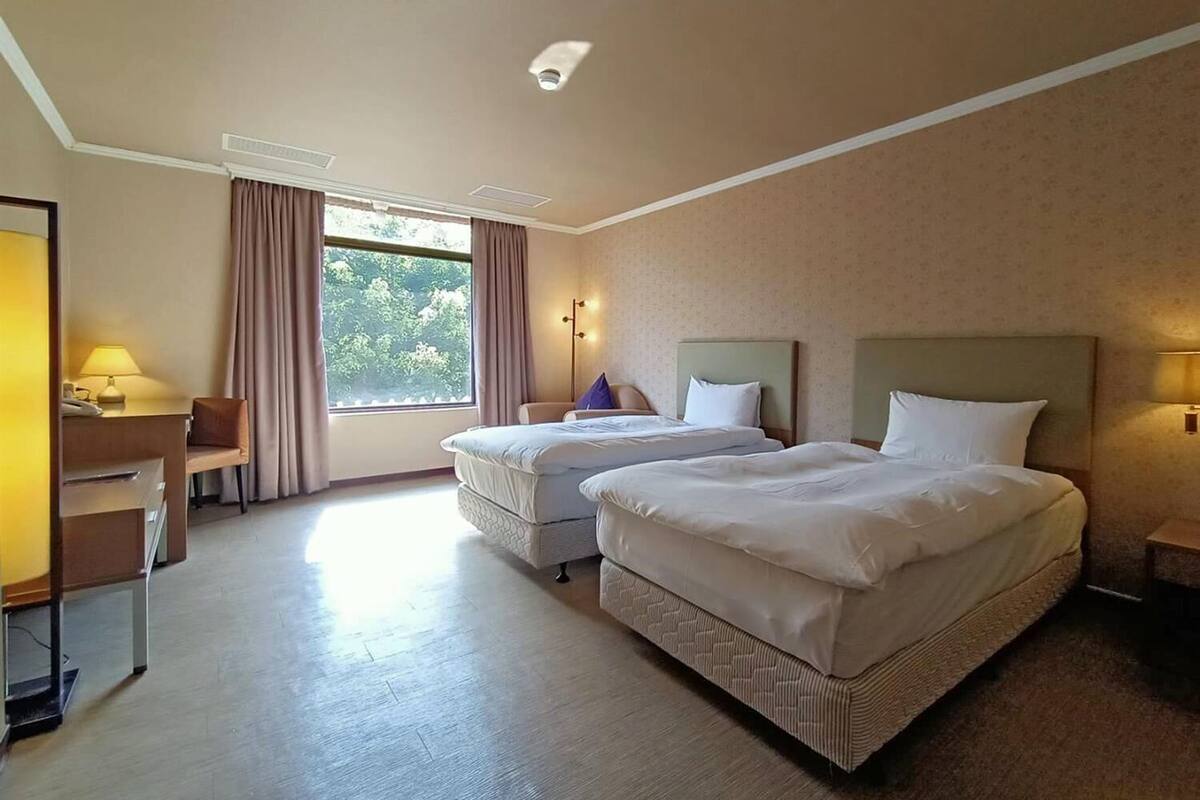 A hotel room with two beds, a desk, and a chair.