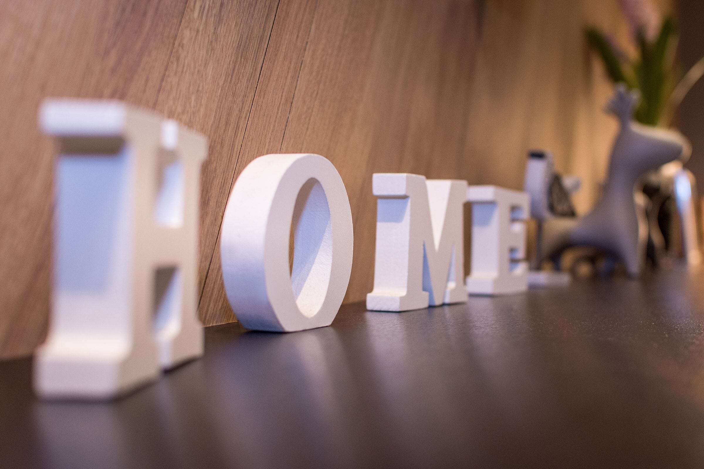 Valkoiset puukirjaimet, joista muodostuu sana ”HOME”, on asetettu puupinnalle.