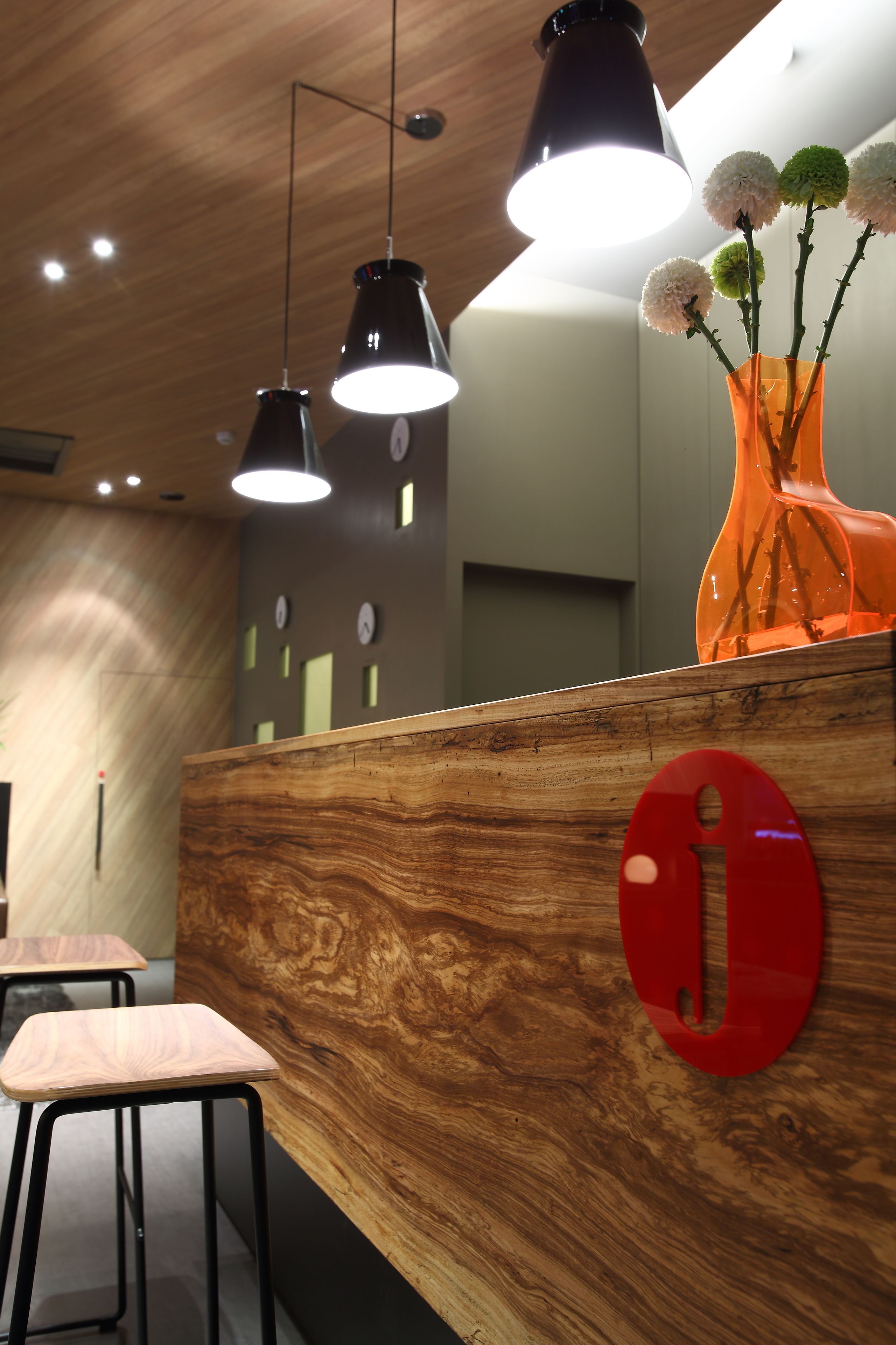 A reception desk with a wooden finish, black pendant lights, and a vase with flowers.
