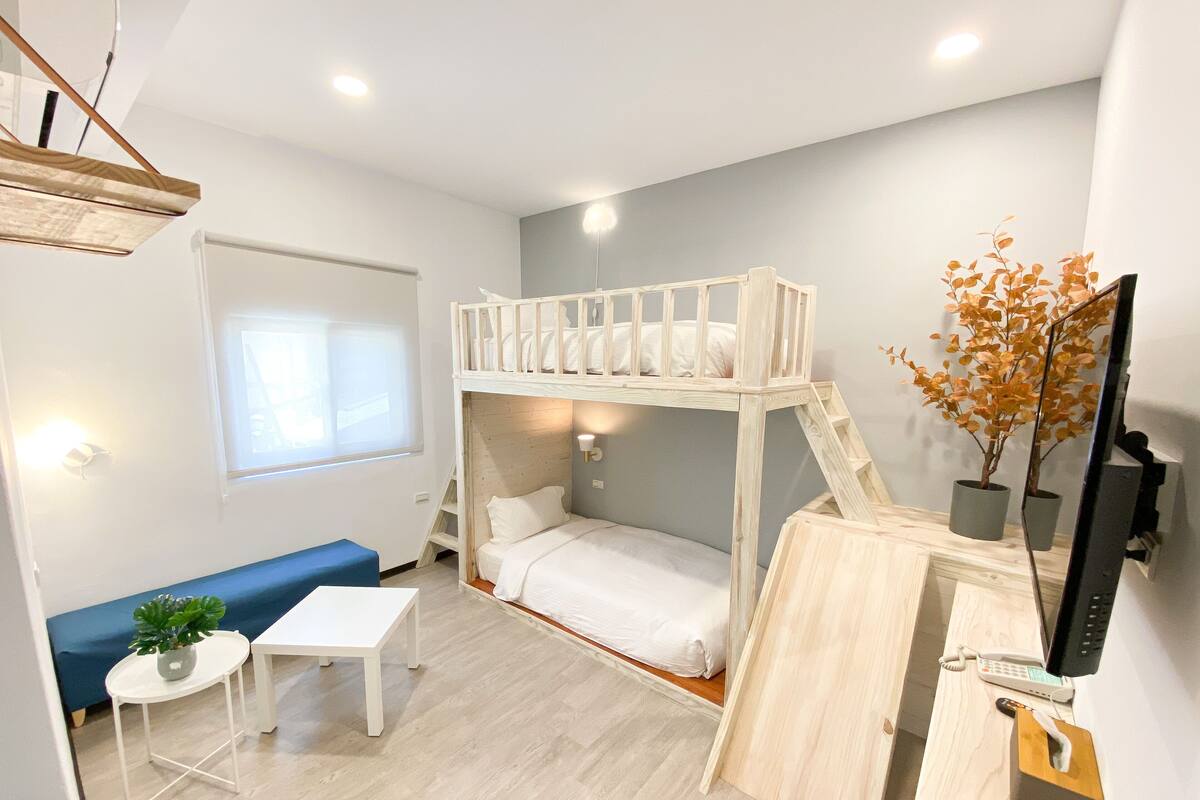 Une petite pièce comprenant un lit superposé, une petite table avec une plante, un canapé et un bureau avec un téléphone.