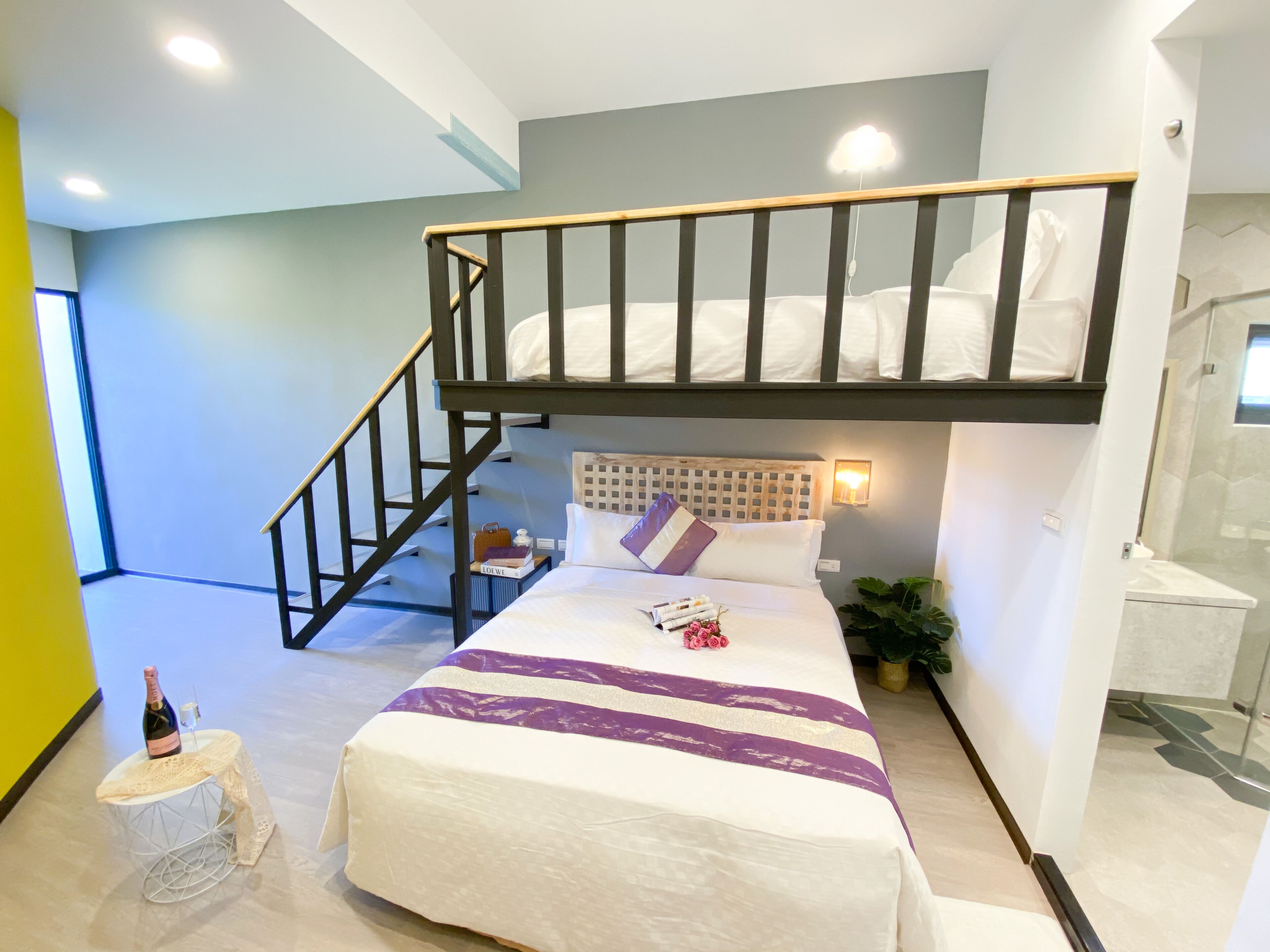 A bedroom with a bunk bed, a small bedside table with a bottle and glasses, a bedside lamp, and a potted plant.