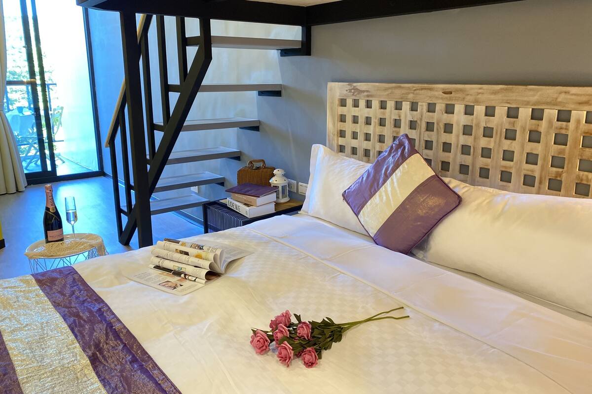 Une chambre à coucher avec un lit, une table de chevet avec des livres, une bouteille de champagne et un bouquet de roses.
