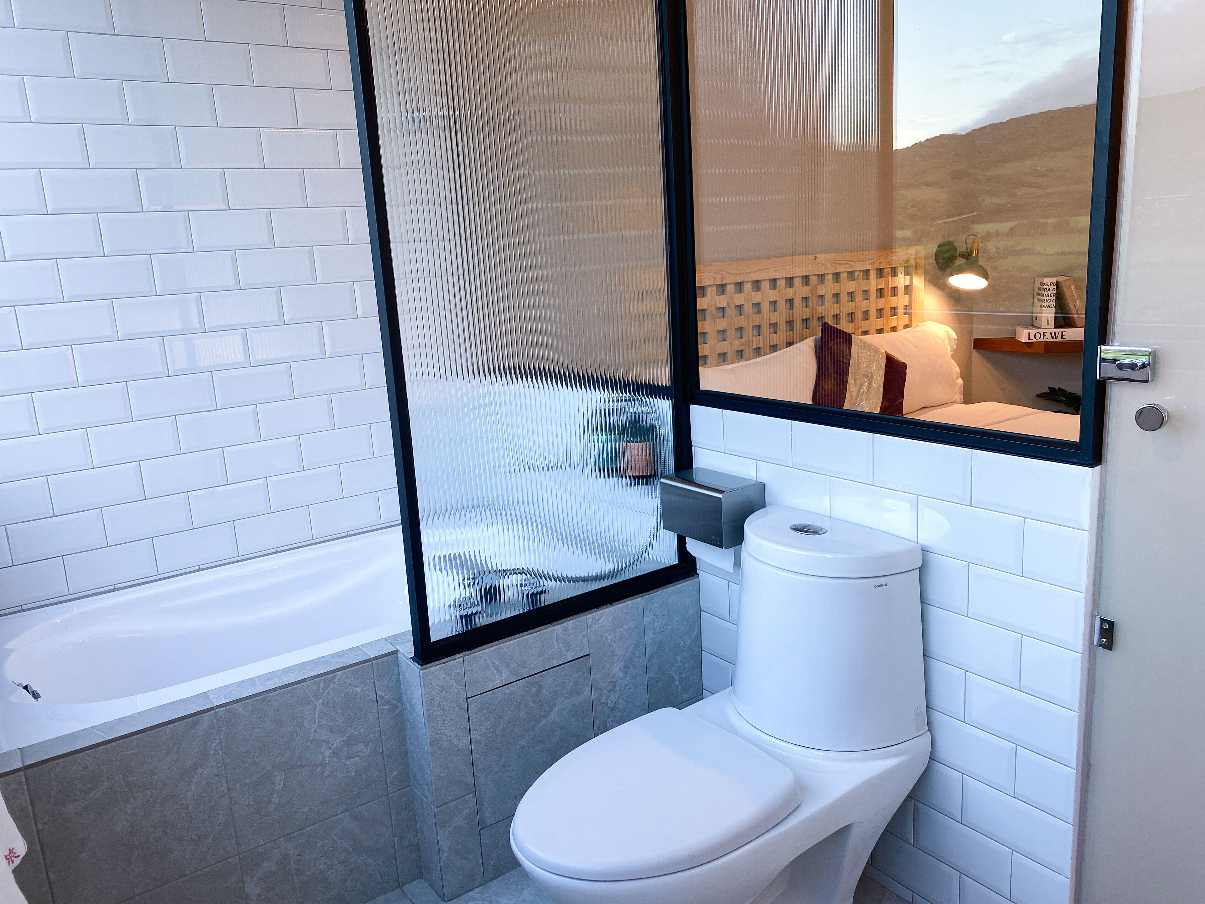A modern bathroom with a toilet, a glass shower enclosure, and a view of a cityscape through the window.