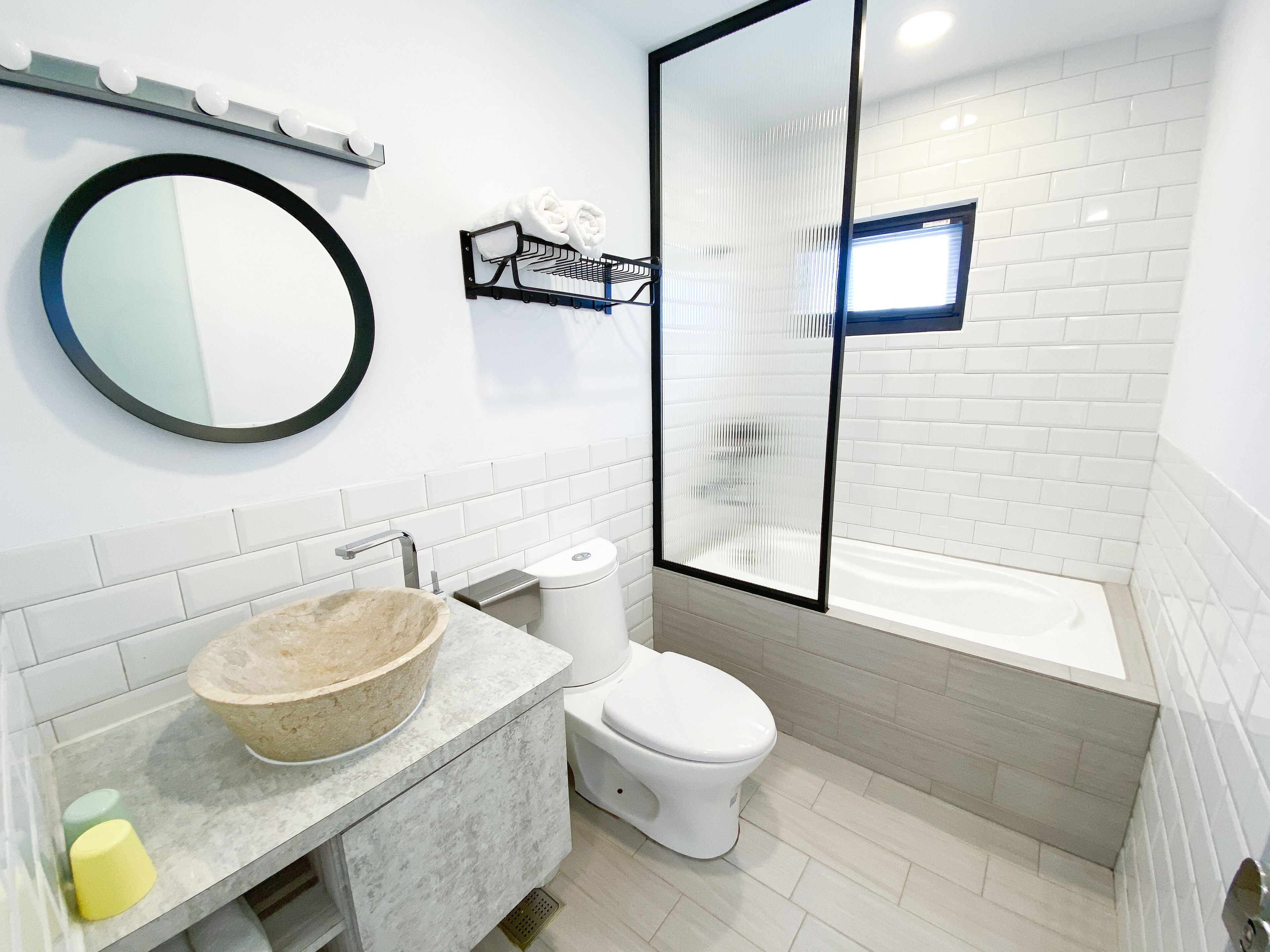 A modern bathroom with a round mirror, a beige sink, a toilet, and a bathtub.