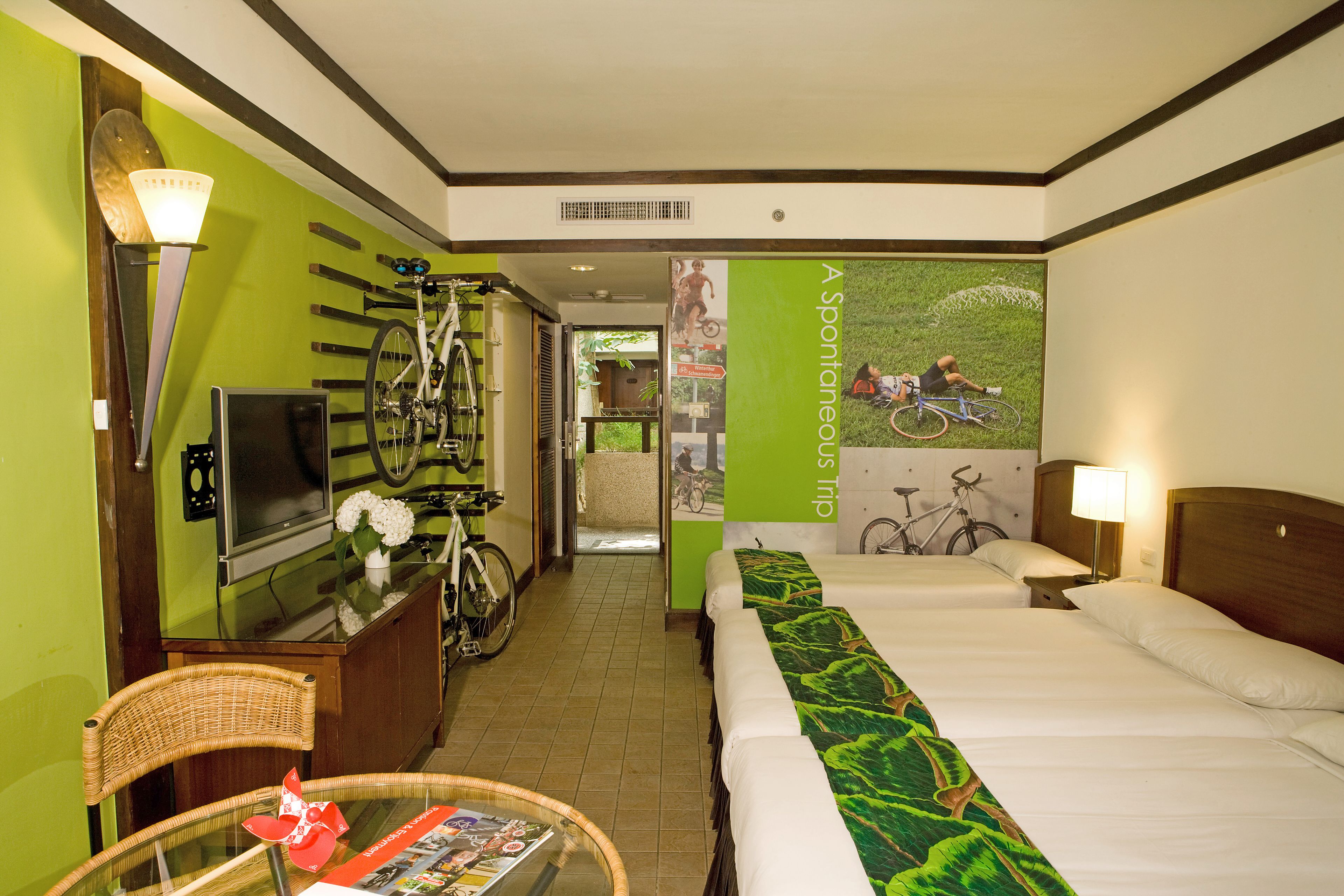 A hotel room with a bed, a television, a bicycle, and a wall with a cycling poster.