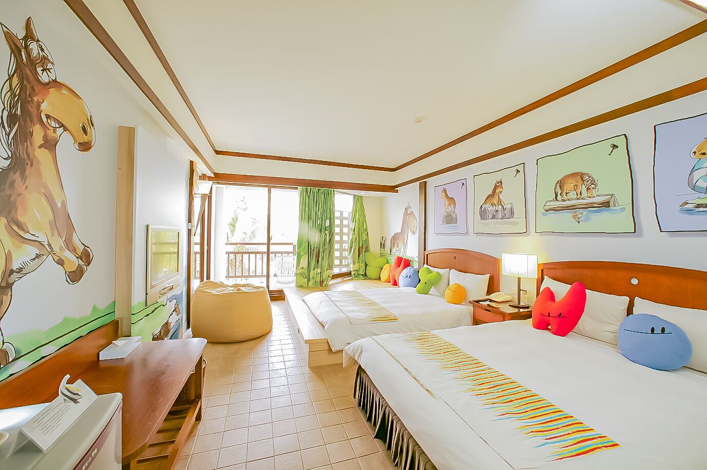 A hotel room with two beds, a wooden desk, a chair, a bean bag, and a balcony with a view.
