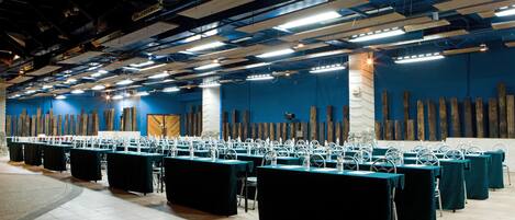 Un salón de conferencias con varias mesas y sillas, una pared azul con paneles de madera y un pilar de piedra.