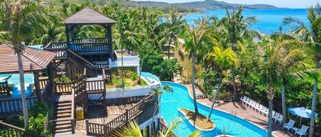 Un resort con piscina, terraza de madera y palmeras.