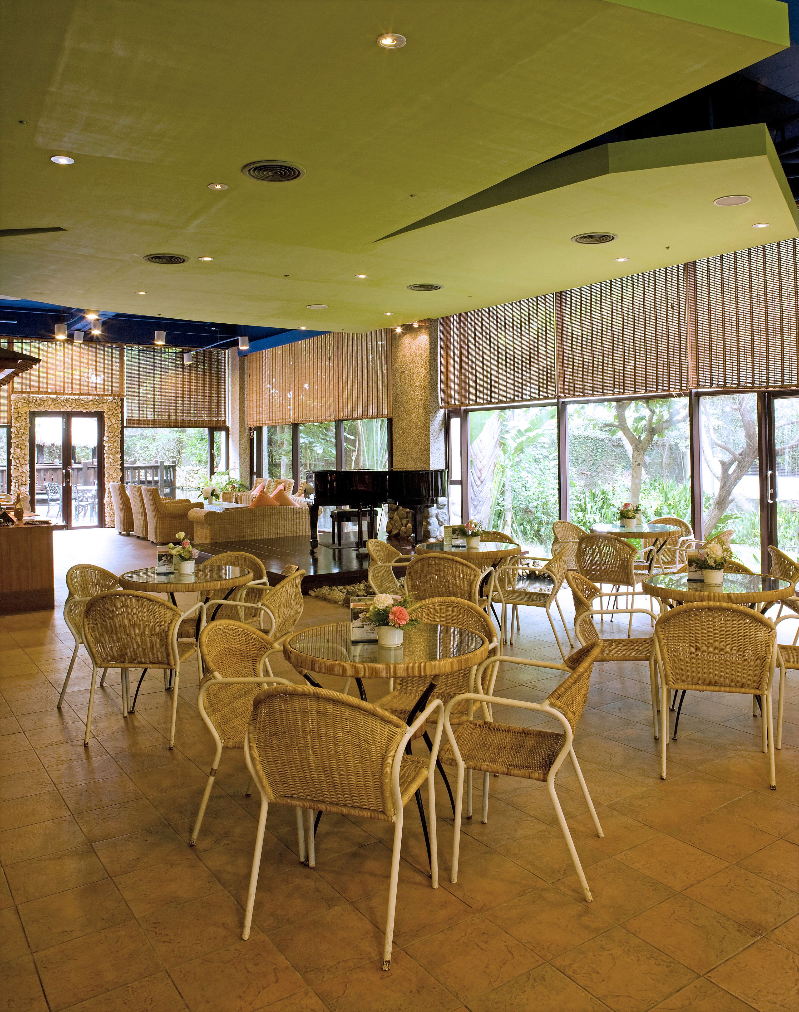 A spacious indoor area with wicker furniture, a piano, and large windows offering a view of greenery.