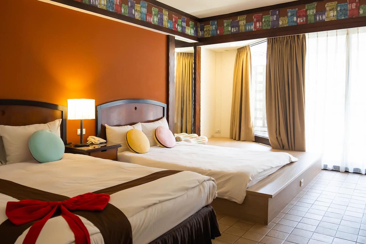 Una habitación de hotel con dos camas, una mesita de noche con lámpara y una ventana con cortinas.
