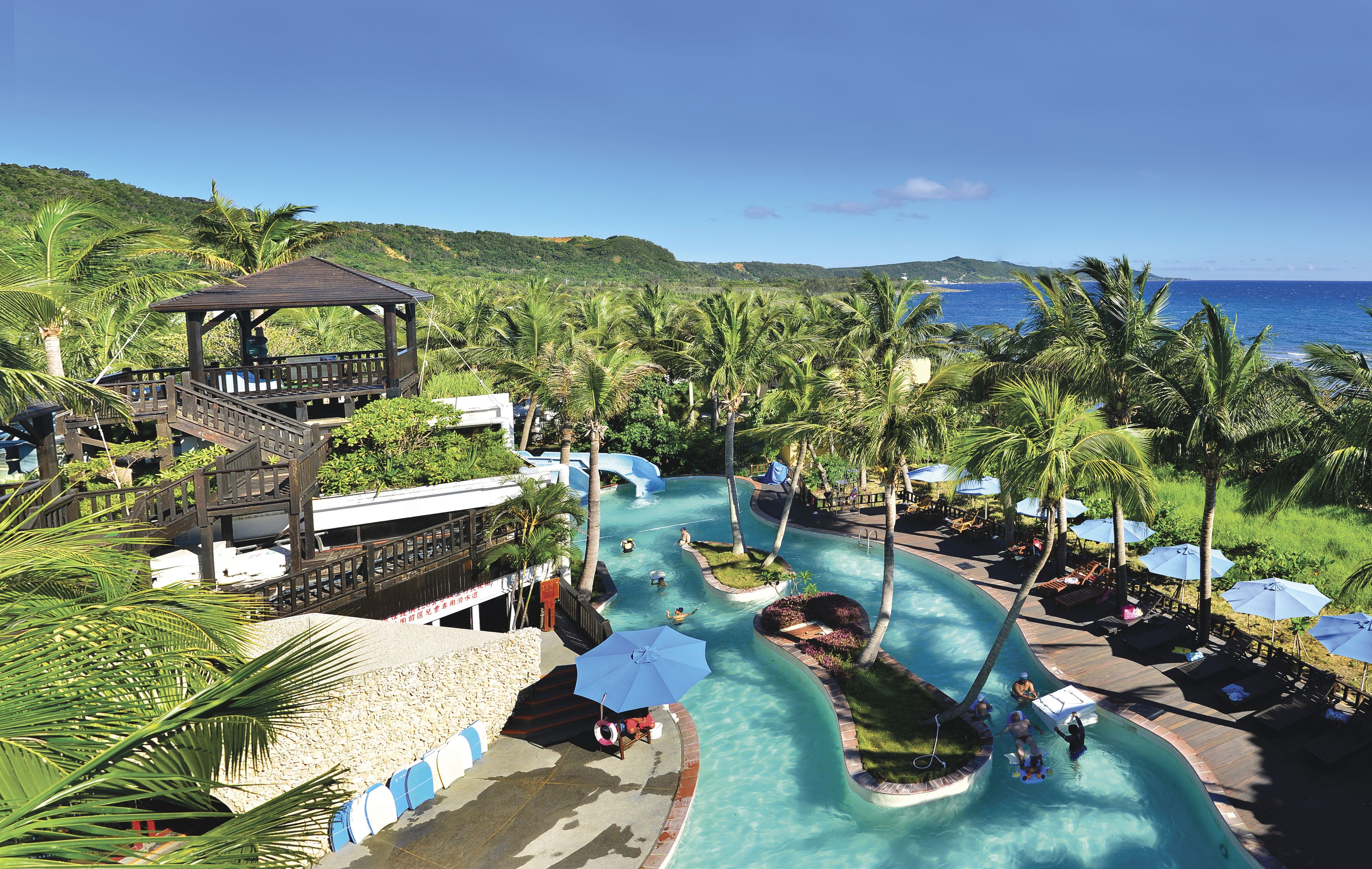 A resort with a pool area, palm trees, and a view of the ocean.