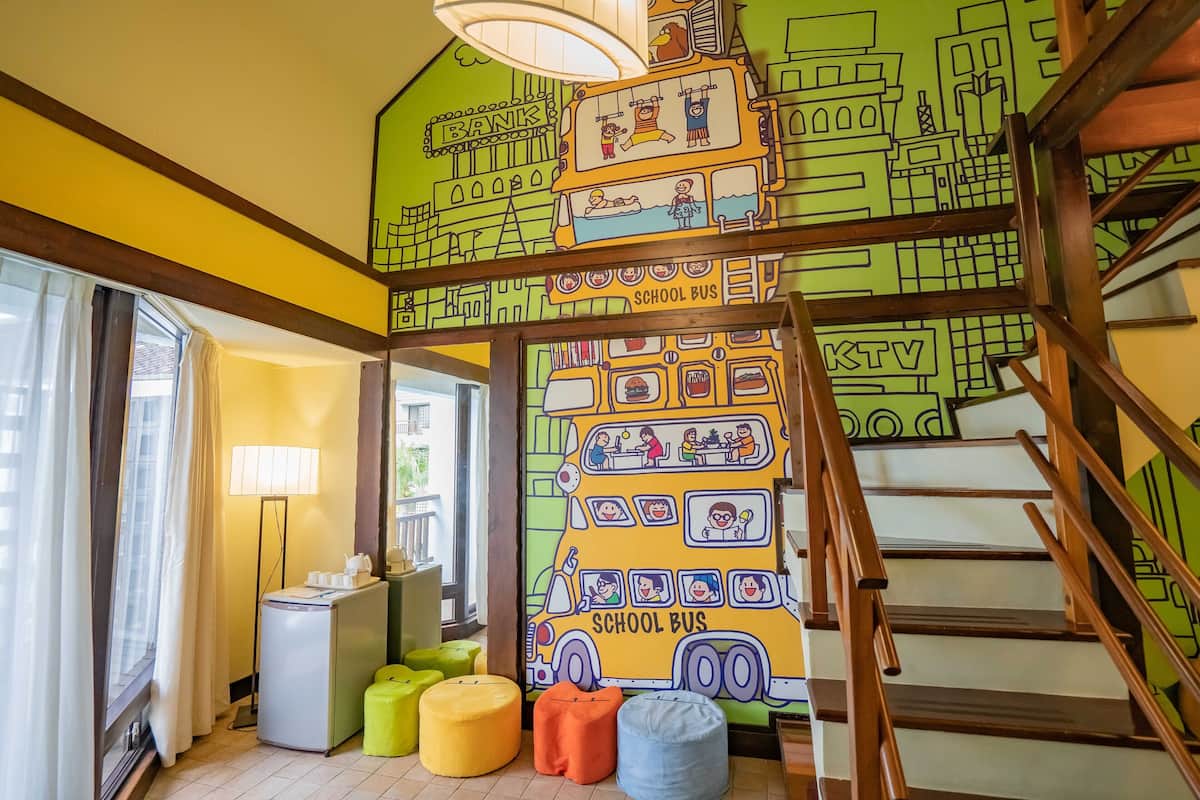 Una habitación de colores vivos con un mural de un autobús escolar y un banco, escaleras de madera y una pequeña kitchenette.