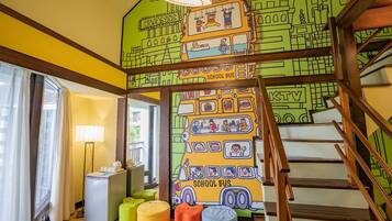 A brightly colored room with a mural of a school bus and a bank, wooden stairs, and a small kitchenette.