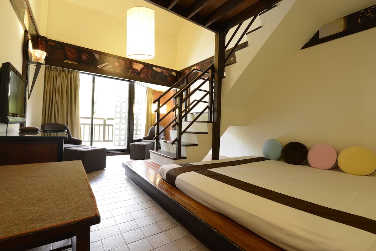 Habitación de hotel con cama, escritorio, sillón, escaleras y vistas al exterior.
