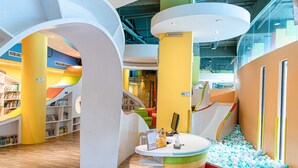 Ein farbenfroher Spielbereich für Kinder mit Bällebad, Bücherregalen und einer Rutsche.