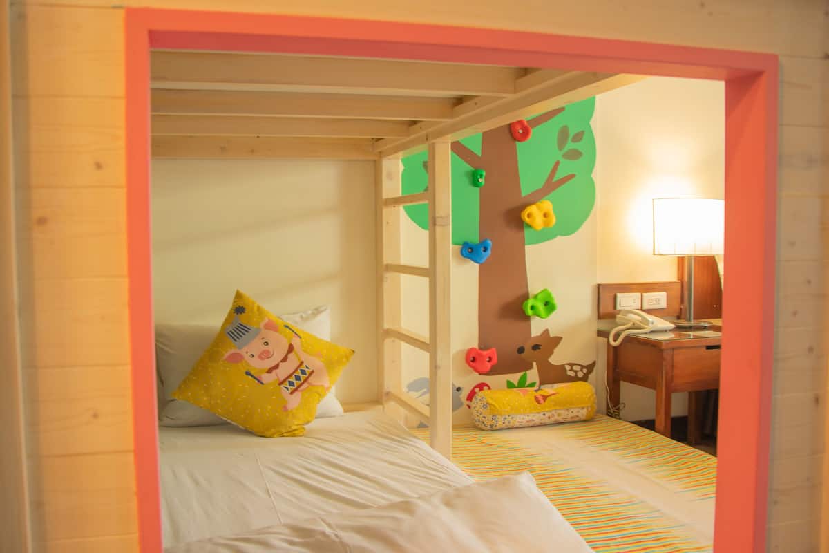 Un dormitorio infantil con literas, una pared de escalar y un escritorio con lámpara.