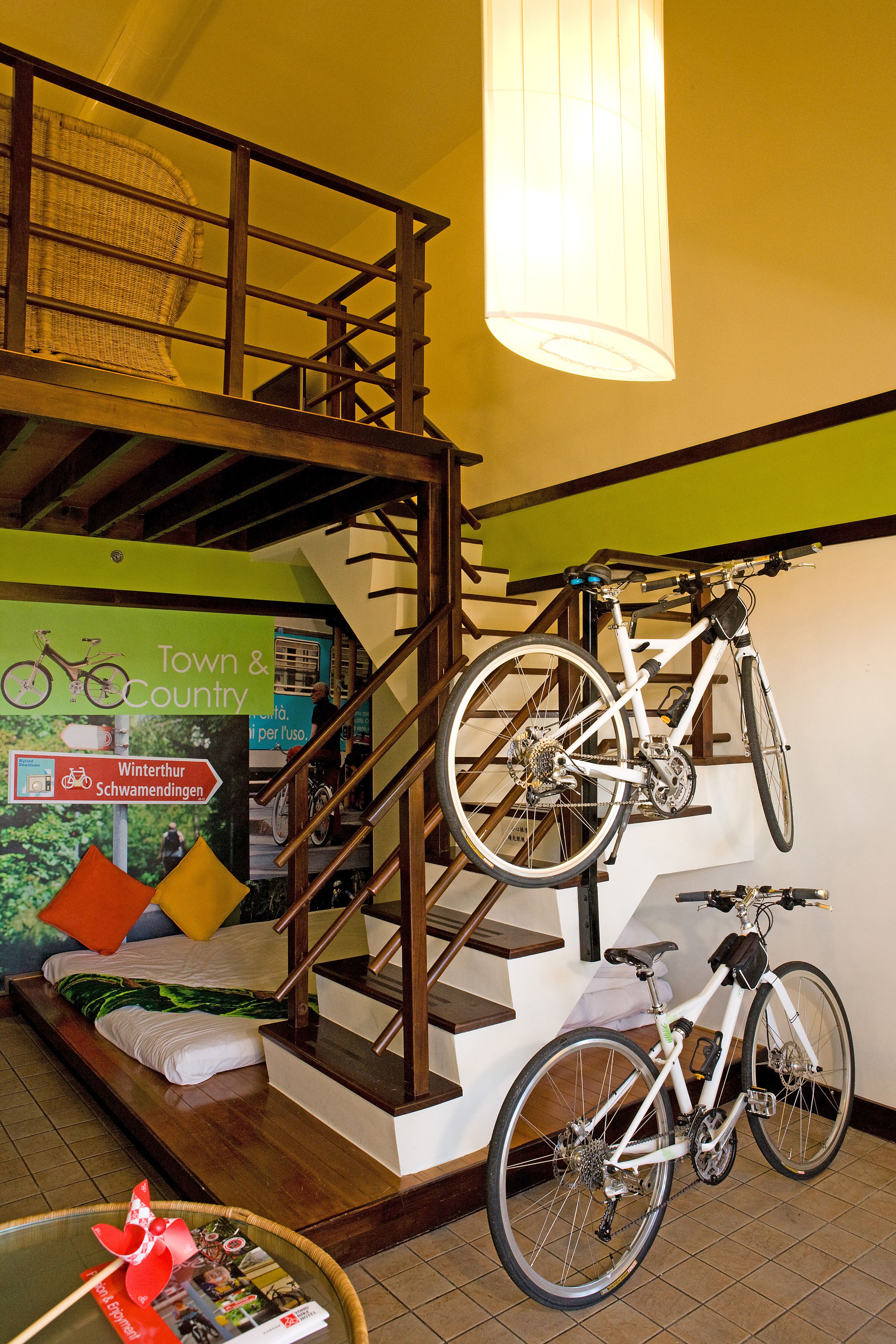 A staircase with a bicycle mounted on the wall, a bed with pillows, and a poster advertising a town and country.