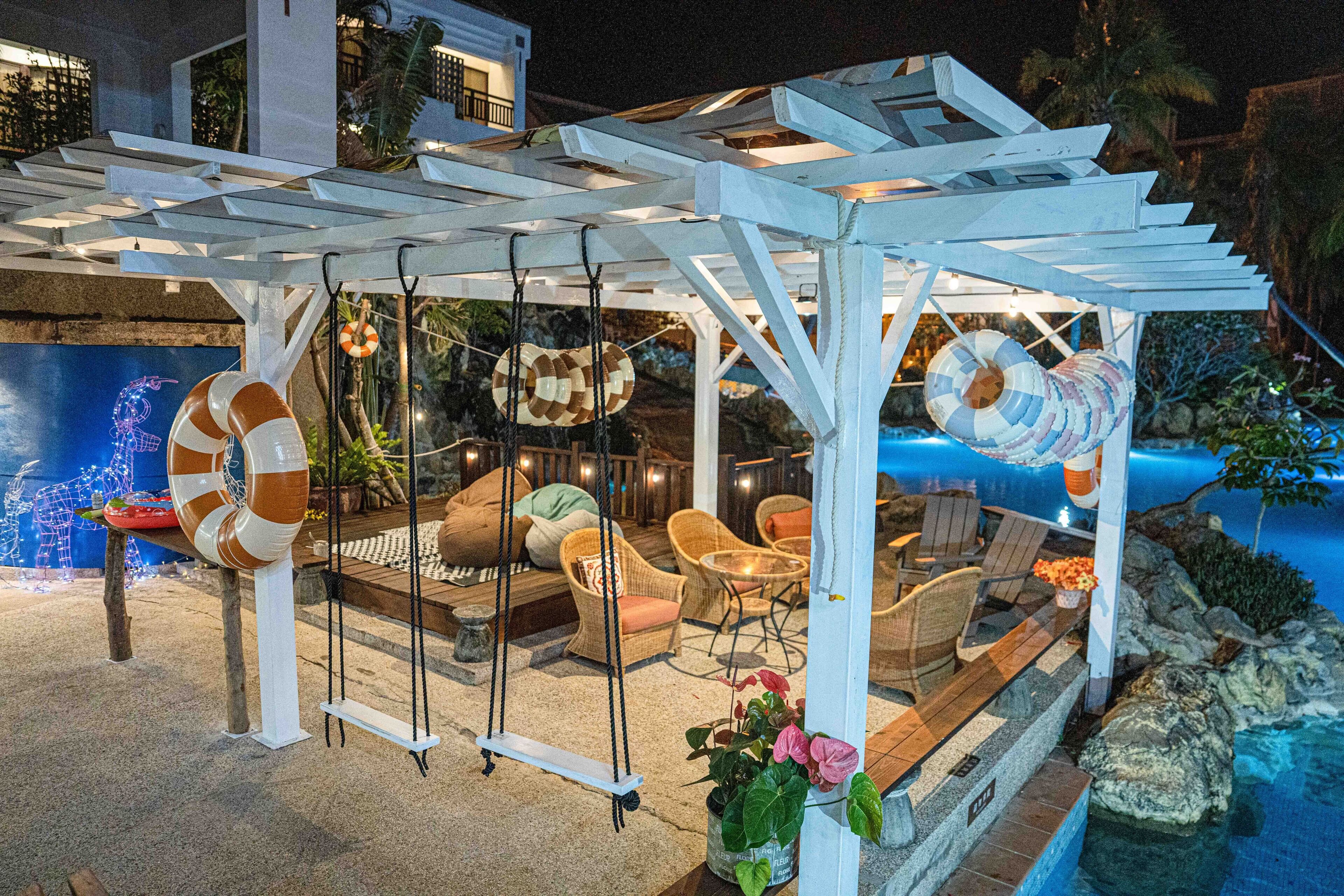 A covered outdoor seating area with wicker furniture and a pool.