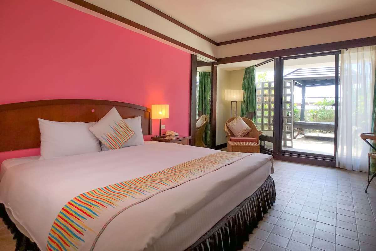 Habitación de hotel con una cama grande, una mesita de noche, una silla y vistas al exterior a través de un ventanal.