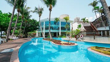 A resort pool area with a large pool, palm trees, and a modern building with large windows.
