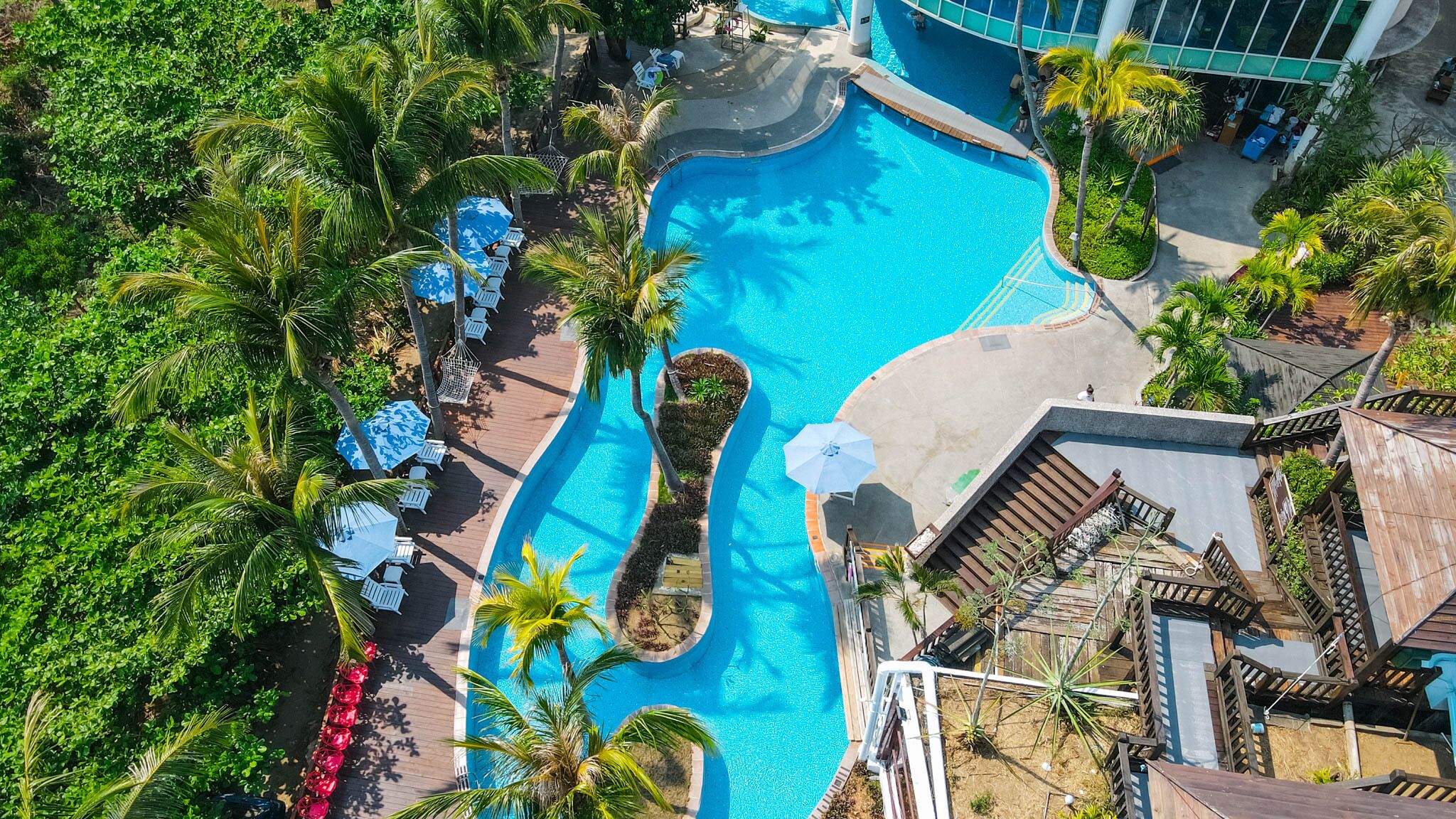 An aerial view of a resort with a large swimming pool surrounded by palm trees and lounge chairs.