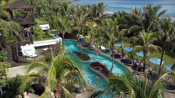 Ein Resort mit Swimmingpool, Palmen und Blick auf den Ozean.