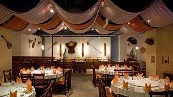 A restaurant with multiple round tables set for dining, featuring orange napkins and white tablecloths.