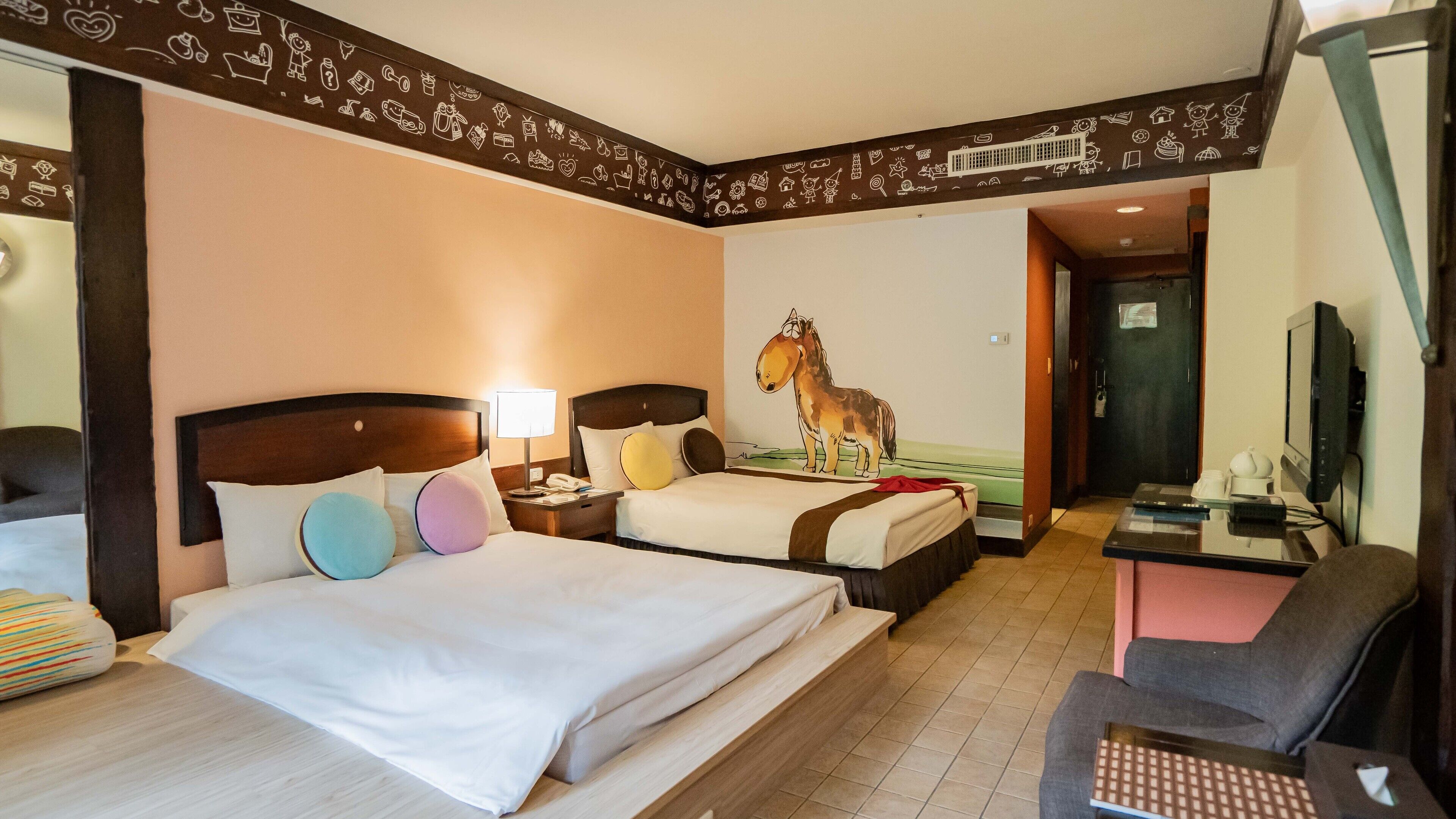 Une chambre d’hôtel avec deux lits, un bureau, une télévision et un mur orné de différents motifs.