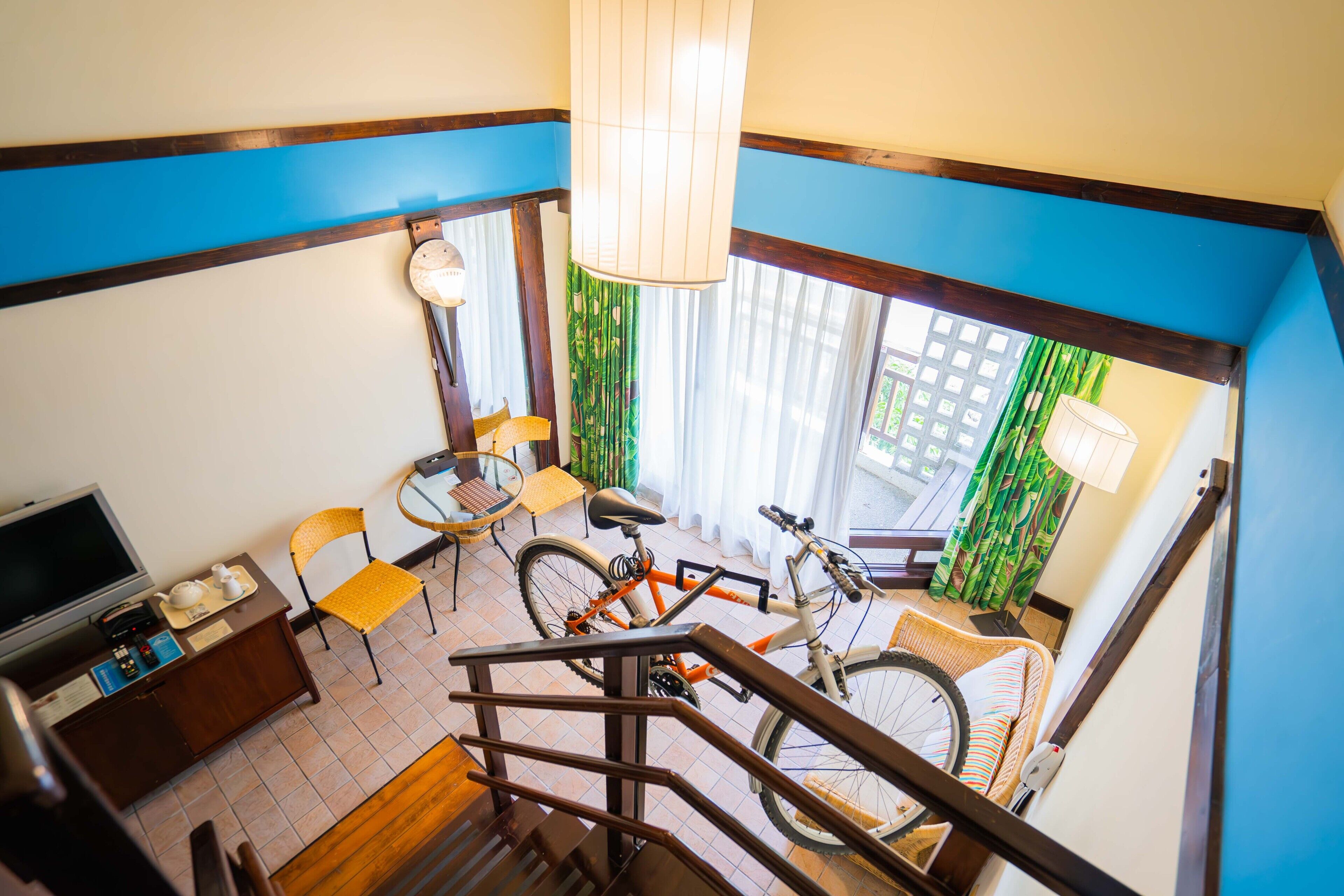 Una habitación con una escalera, un comedor con sillas y una mesa, una bicicleta y un televisor.