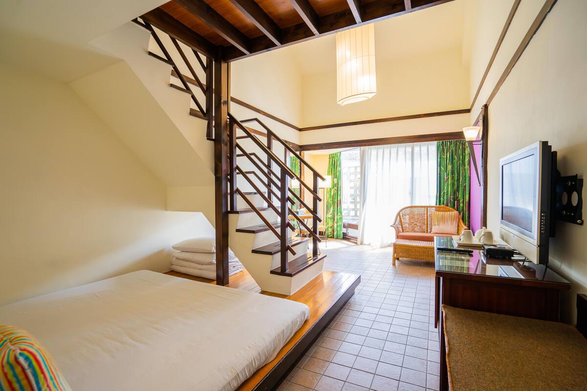 Habitación de hotel con cama, escritorio, televisión, escalera y vistas al exterior.