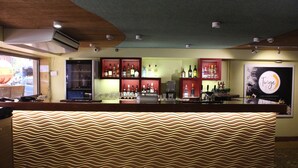 A bar area with a wavy patterned counter, shelves with bottles, and a sign that reads "Tunge". - Grande Delmon (Panaji)