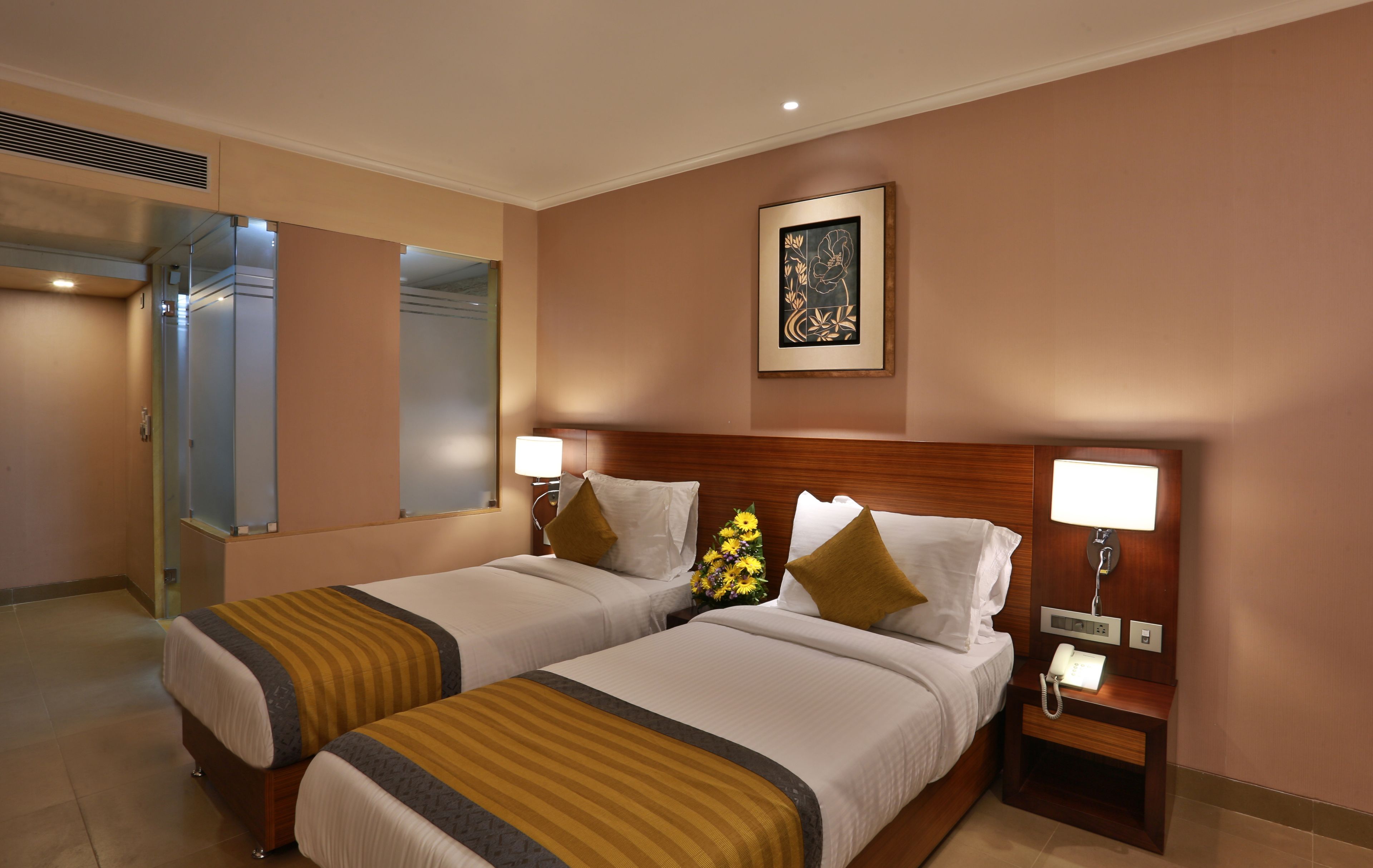 A hotel room with two beds, a wooden headboard, bedside lamps, a telephone, and a framed artwork on the wall.