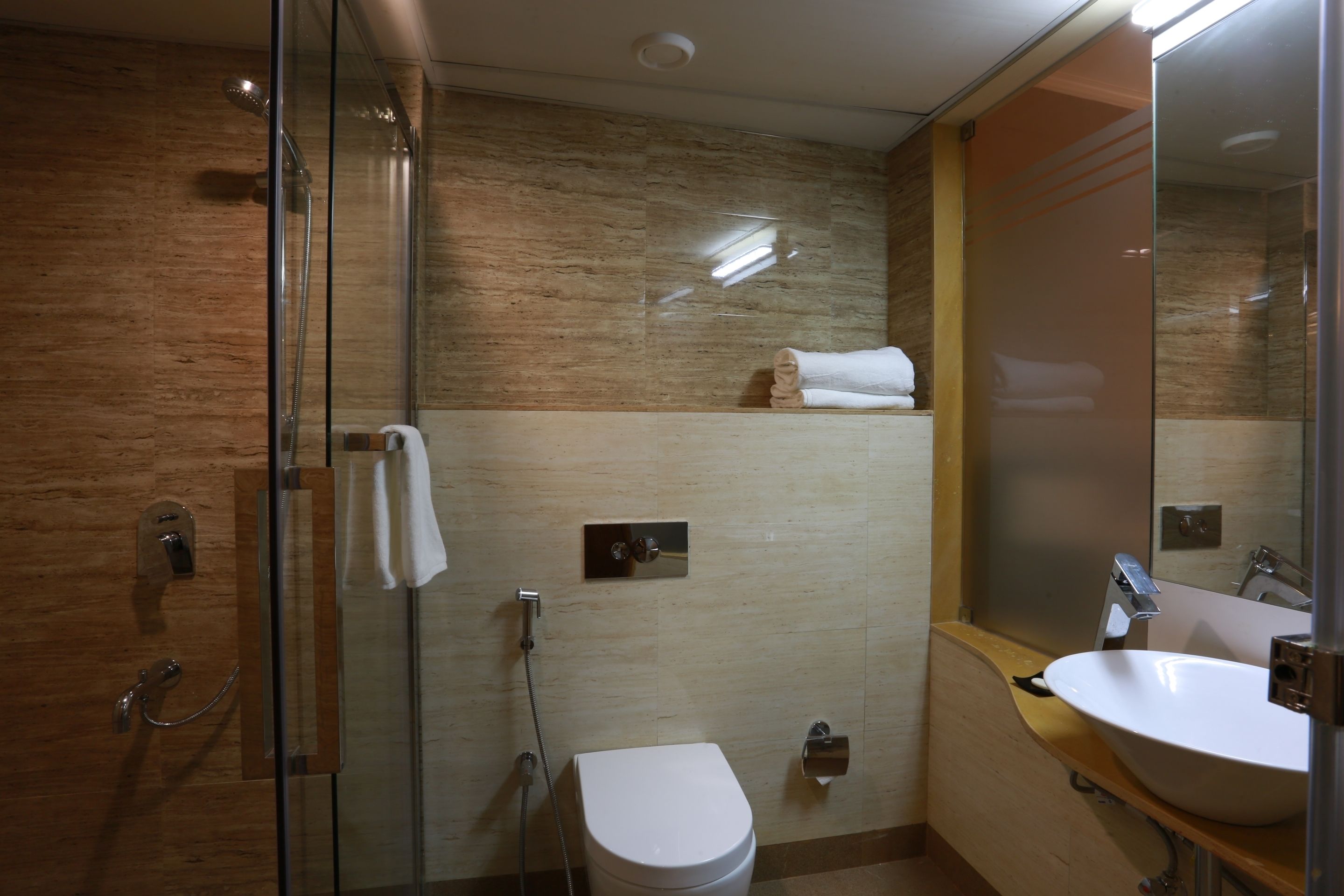 Un baño moderno con cabina de ducha de vidrio, un inodoro blanco, un lavabo con espejo y un perchero para toallas.