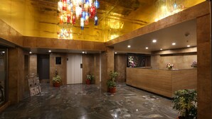 A lobby with a reception desk, potted plants, a marble floor, and a colorful chandelier. - Grande Delmon (Panaji)