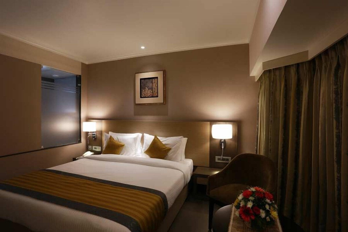 A hotel room with a large bed, two bedside tables with lamps, a chair, a framed picture on the wall, and a curtain.