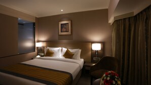 A hotel room with a large bed, two bedside lamps, a nightstand, a chair, and a framed picture on the wall. - Grande Delmon (Panaji)